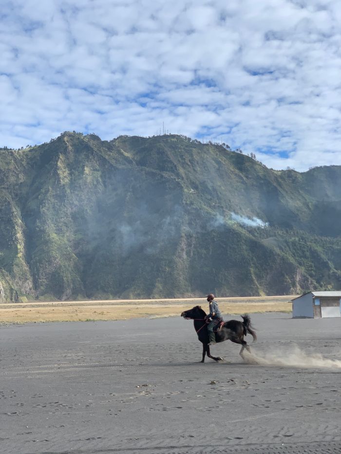 Man riding a horse across the sandy plains of Mount Bromo in Indonesia.